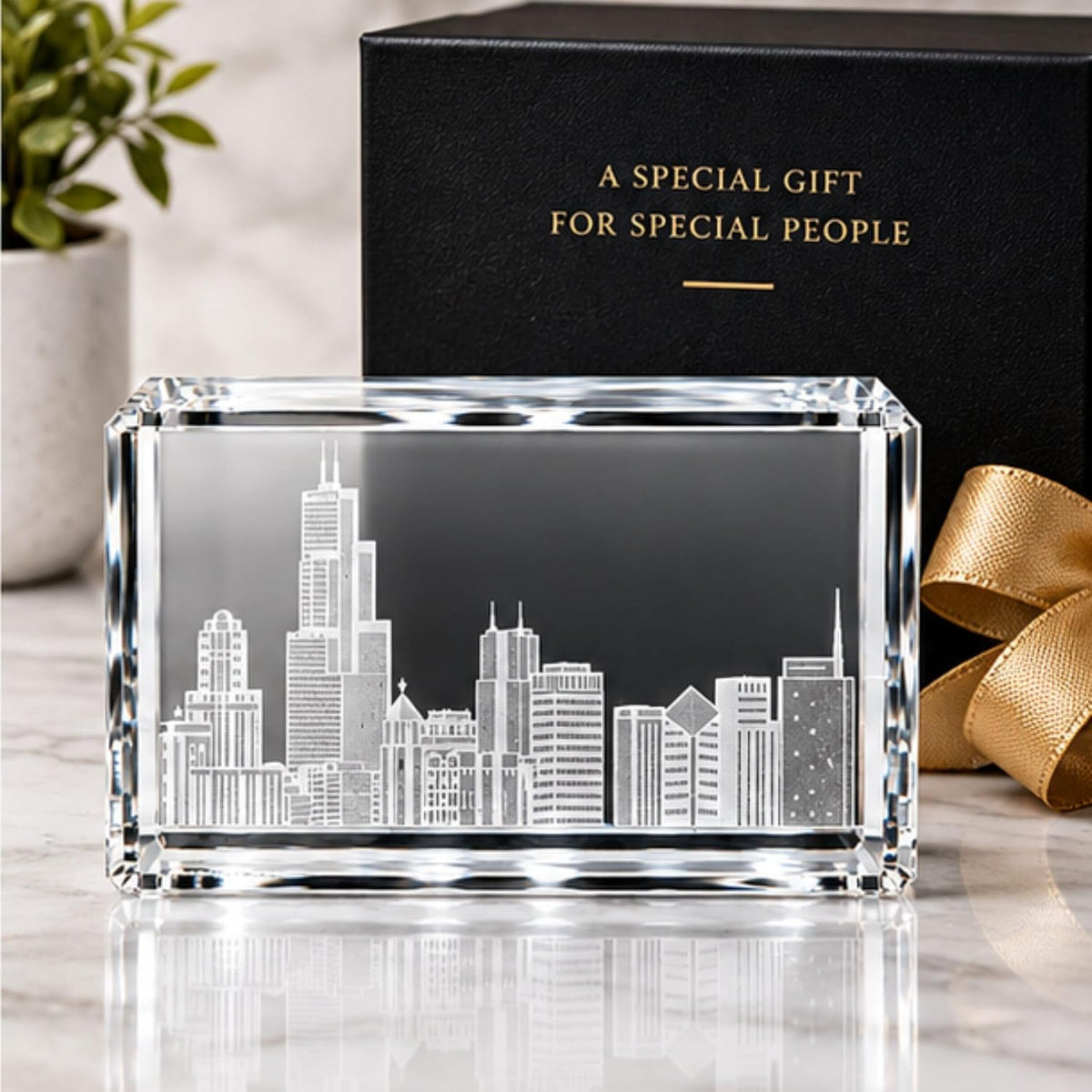 A rectangular clear crystal or glass plaque featuring an etched white skyline design, displayed on a light marble surface with a black gift box and gold ribbon in the background.