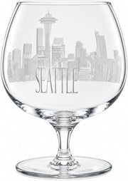 Clear glass snifter wine glass featuring an etched grayscale Seattle skyline and the word 'SEATTLE' on the bowl, shown on a white background.