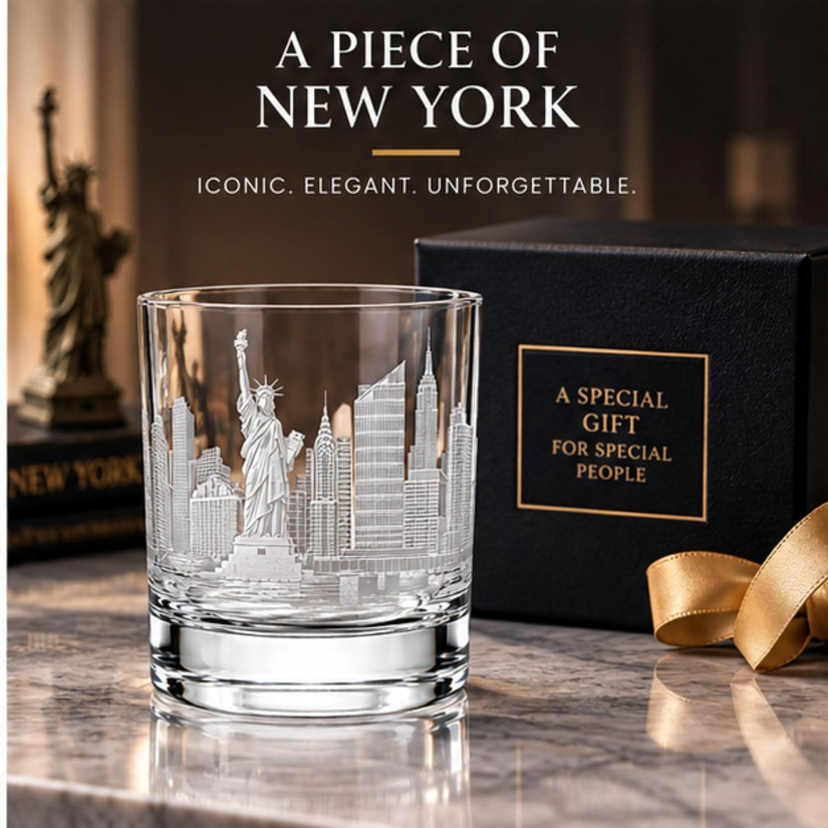 A clear engraved tumbler glass featuring a New York City skyline design with the Statue of Liberty, shown on a marble surface beside a black gift box with gold lettering and a gold ribbon. Large text at the top reads 'A PIECE OF NEW YORK' and 'ICONIC.