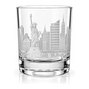 A clear glass rocks tumbler featuring an etched New York City skyline design with the Statue of Liberty and skyscrapers, shown on a white background with a soft reflection.